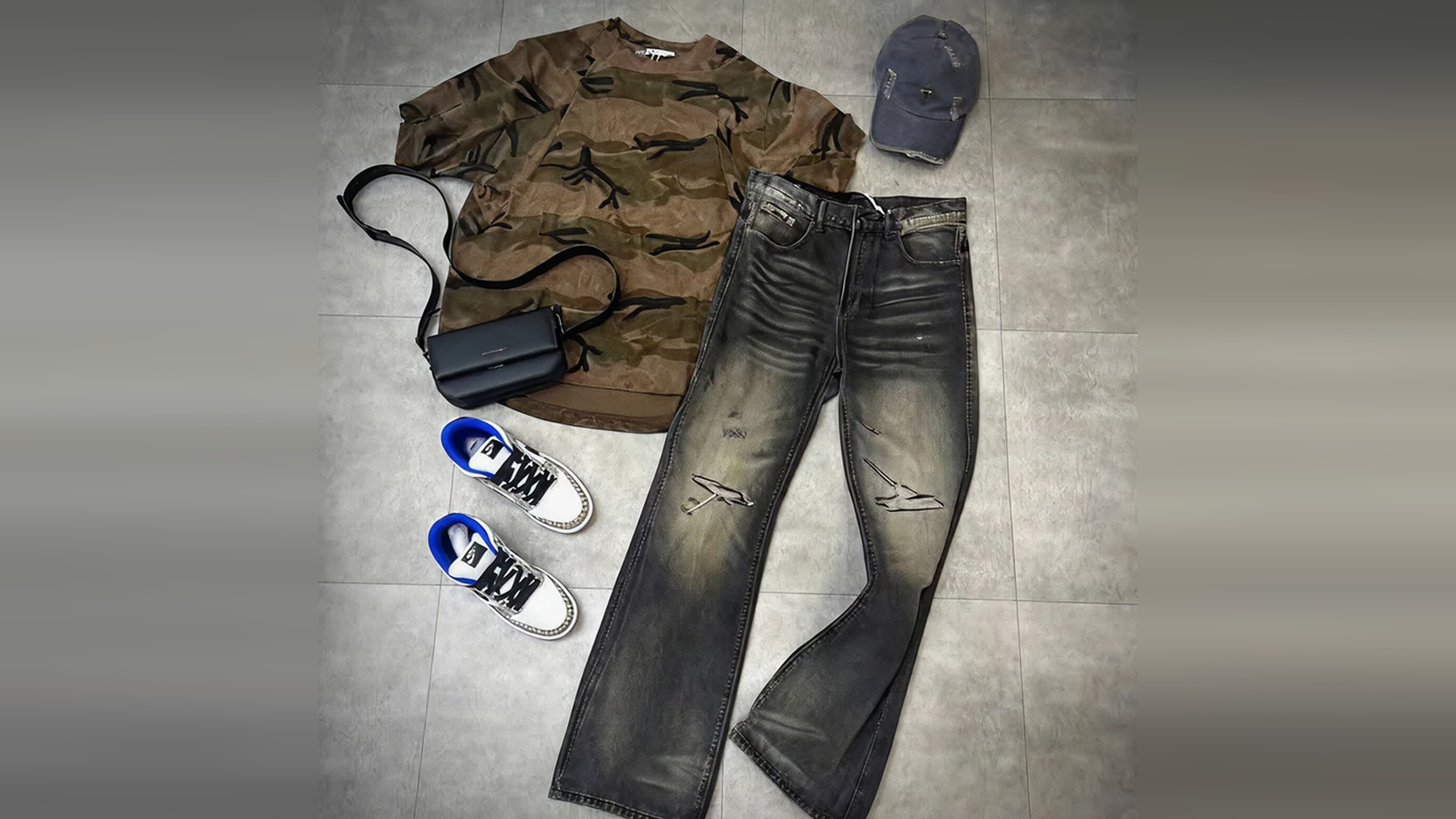 Before: the product photo the workflow starts from, a camo T-shirt, washed flared jeans, a cap, a bag and sneakers laid flat on a grey floor